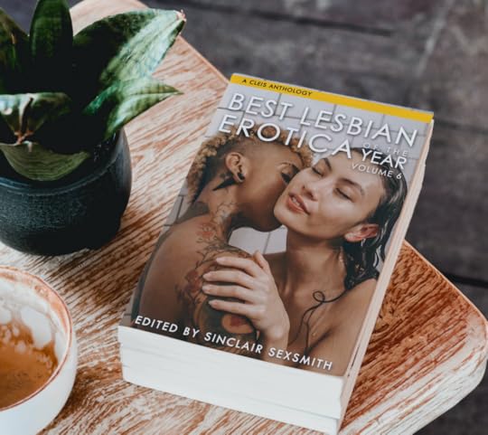 The cover of Best Lesbian Erotica Volume 6 sitting on a wood table next to a succulent plant and a white-and-brown ceramic bowl