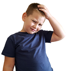 A boy in a dark blue shirt rubs his head and looks confused and distressed.