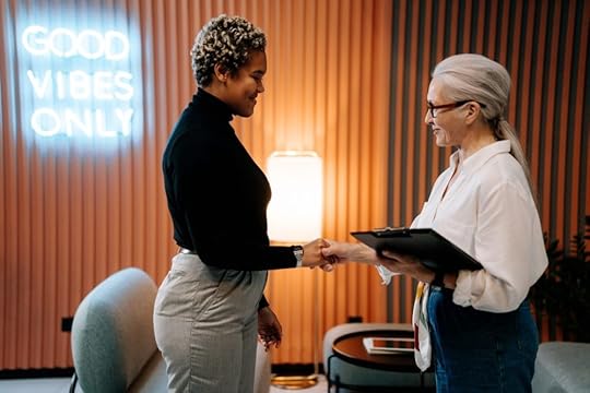 Image: two professional women shaking hands. A neon sign on the background wall reads 