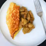 wedge of puffed pancake on plate topped with apples, a fork is nearby.
