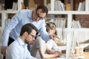 Man standing over coworker's shoulder being annoying
