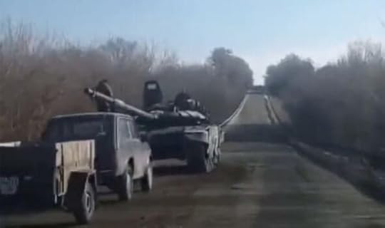 A broken down tank at the side of the road. In front of it sits an old Lada - an eastern European car covered in mud and dust, with a little trailer attached.