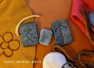 The Elder Futhark rune Tiwaz carved into wrought iron, Fehu in silver clay, and Ingwaz in iron, with a mink rib, on a mixed color background