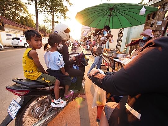 Scene of street food in Siem Reap with people on scooters ordering meals.