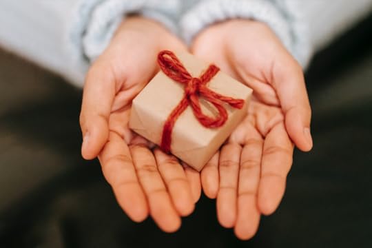 Image: a woman's open hands holding a small, wrapped gift.