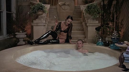 Amanda Donohoe sitting and smoking on the edge of a bathtub in lingerie, about to kill an unsuspecting young man, in Ken Russell’s