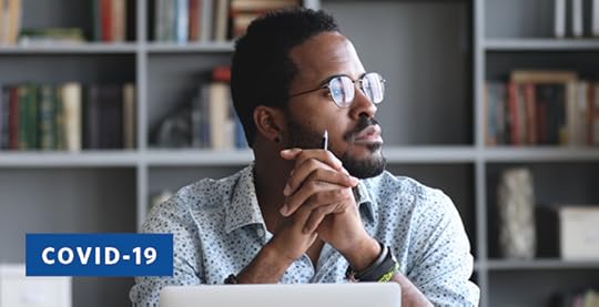 African American student with beard and glasses in front of a bookcase with a computer on his desk stares out the window in a distracted fashion.