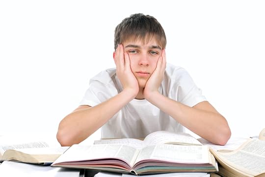 photo of a teen boy with many open books in front of him looking bored and tired.
