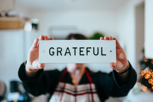 Photo of person holding white sign with black letters. Sign says GRATEFUL.