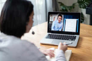 Woman interacting through her computer with a man at a whiteboard