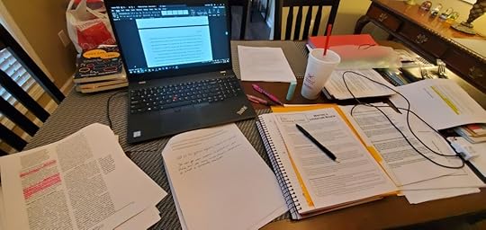 A table full of research articles, notebooks, and a laptop.