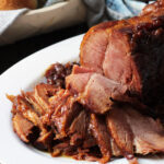 sliced holiday ham on white oval platter.