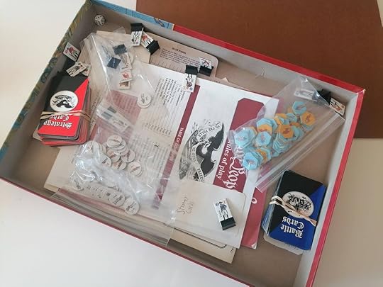 The inside of the large box, only partially filled with an assortment of bagged cardboard chits, plus two decks in rubber bands. The box sits atop the folded game board.