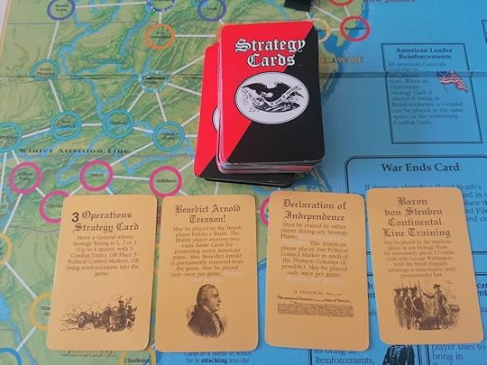 A deck of Strategy Cards set atop the game board. Four cards are laid out face up - one generic operations, one called Benedict Arnold Treason!, one Declaration of Independence, and a Baron Von Steuben card.