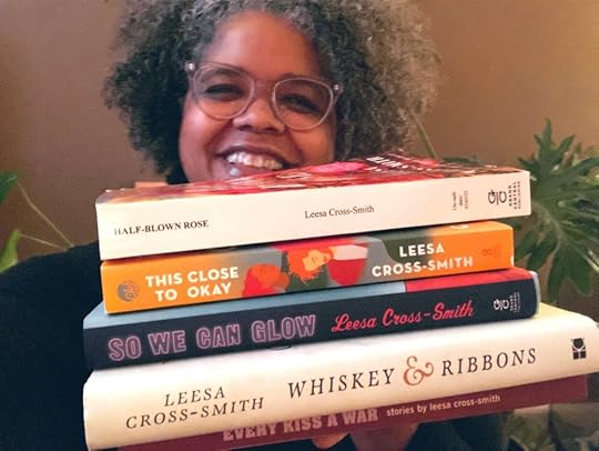 Author Leesa Cross-Smith, smiling, holds copies of all five of her books