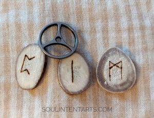 Elder Futhark runes Mannaz, Isa, Perthro, on a white and beige striped background with a tiny metal wheel.
