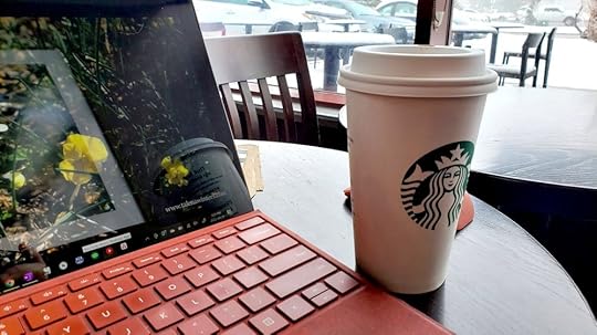 Picture of open laptop and Starbucks coffee cup on a cafe table in front of a window with snow outside.