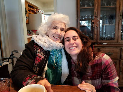 Photo of Gina and Gena cheek to forehead at a table with a walker and cabinet behind them