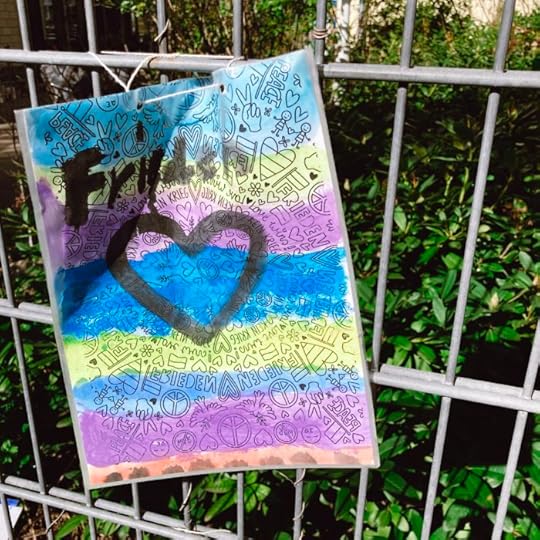 Ein von Kindern gemalter Zettel an einem Zaun: Das Wort Frieden mit einem Herz darunter