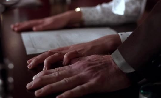 Three white hands palm-down on a desk. Still from Secretary (2002)