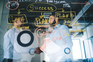 Two people discussing a process flow shown on a whiteboard