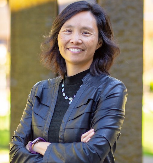 Judy Wu stands, arms folded, outside on a sunlit day, for a half-length portrait