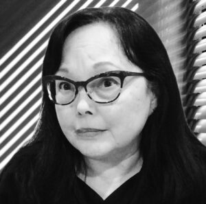Black and white head shot of Wendy Mink, wearing glasses, with striped shadows from a window shade behind her