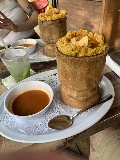 A wooden chalice contains mashed plantains and chicken alongside a soup.