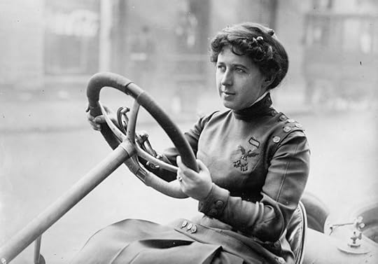 Black and white photo of woman behind the prominent steering wheel of an open car