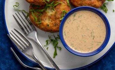 Three potato fish cakes on a plate with remoulade sauce.