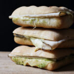 stack of three turkey pesto sandwiches on wood cutting board.