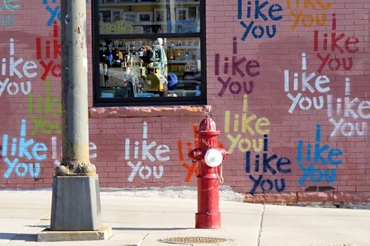 Image: an urban brick wall on which are painted many colorful versions of the phrase 