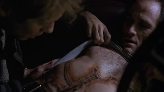 James (James Spader) examines the “prophetic” tattoo on Vaughan’s (Elias Koteas) abdomen. The tattoo is appropriately Cronenbergian in its ugliness. 