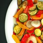 overhead closeup of roast vegetables on white platter on black table.