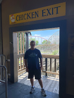 A teenager stands silhouetted in a doorway with a rollercoaster in the background. A sign above the door reads