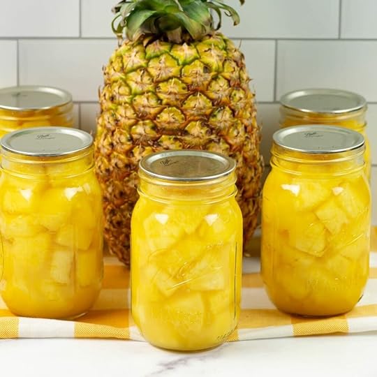 Pint canning jars filled with canned pineapple chunks with a whole ripe pineapple in the background.