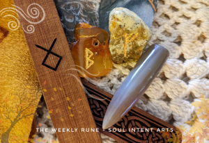 Elder Futhark runes Fehu and Berkana carved into Baltic amber pieces, with Othala reversed pyrographed into a sanded cedar stick, with Fossilized Belemnite on an offwhite crocheted background.