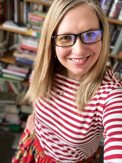 A selfie of a 41 year old white woman with long blonde hair wearing a red and white striped top and black-framed glasses . She's smiling.