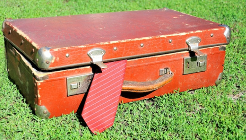 Suitcase on grass, with tie peaking out