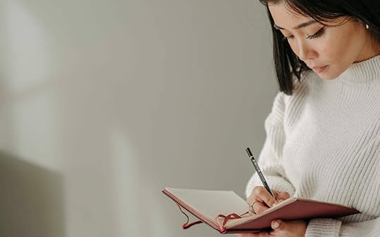 a woman is writing notes on a pink note book