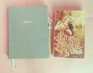 Two books lie side by side. One is an A5 size cloth covered notebook in sage green, with the word 