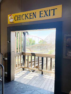 An open doorway with a rollercoaster in the background. Above the doorway is a yellow sign that reads,