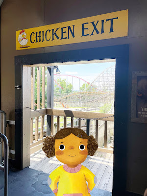 Wanda, a cartoon girl with dark skin and brown hair in a yellow and pink sweater, stands in a real life doorway with a rollercoaster in the background. Above the doorway is a sign that says
