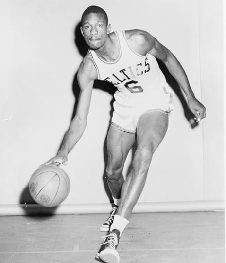 A young Bill Russell dribbling the basketball for a publicity photo in front of a white wall.