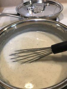 A small saucepan containing milk, vanilla beans, and sugar that has thickened slightly