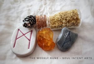 Elder Futhark runes, including Thurisaz carved into silver clay with blue paint, Kenaz carved into Baltic amber, and Mannaz carved onto a porcelain tile, currsounded by a small silver pinecone and a small vial of lemon zest, all on a cream-colored background