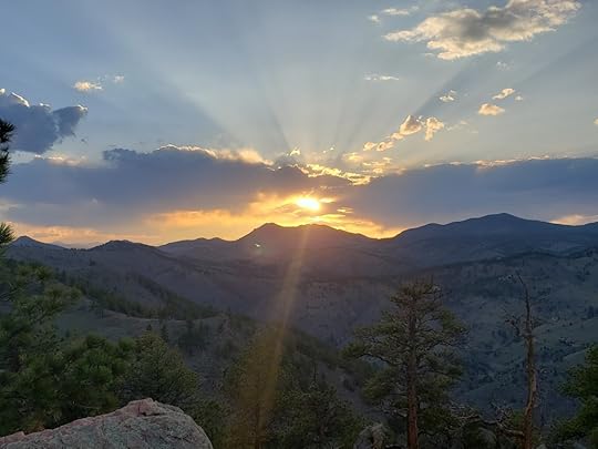 Rays of sunshine radiate from a setting sun in the Rocky Mountains of Colorado. A jagged line of mountain ridges form the horizon. (Photo by TJ Burr, 5/7/2021)