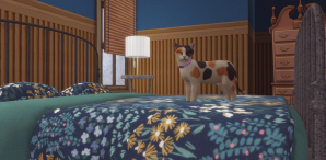Screenshot from the video game The Sims 4. A calico cat stands atop a metal framed bed, covered in blue flowered bedding. 