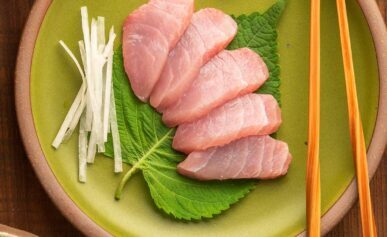 Hamachi sashimi on a plate with shiso, wasabi and julienned daikon radish.