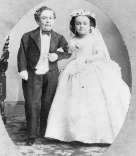 A bride and groom, both dwarves, pose arm in arm for a wedding photo